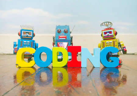 the word coding wit wooden letters on a old wooden floor with retro robot toysの写真素材