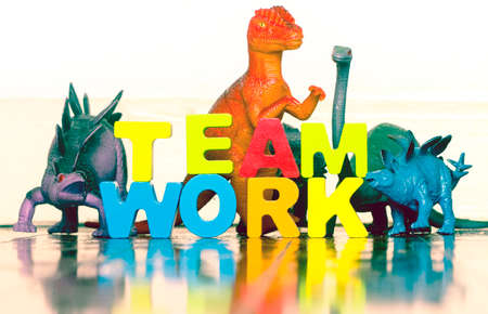 The word TEAM WORK with wooden letters and 5 toy dinosaurs on a wooden floorの写真素材