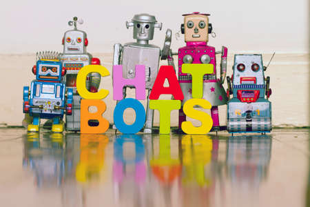 The word  CHAT BOTS with 5 retro robots on a wooden floor with reflectionの写真素材