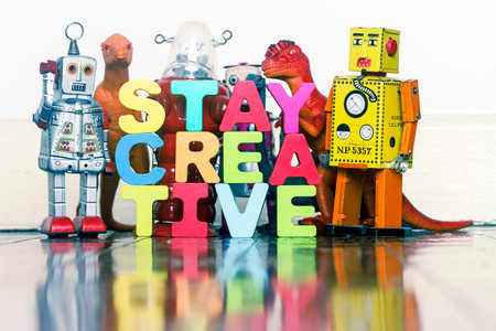 The word STAY CREATIVE with wooden letter, dinosaurs and robots on a wooden floor with reflectionの写真素材