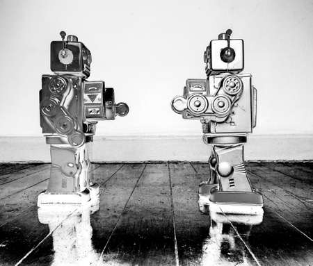 two retro robots face off with ray guns on a wooden floor with reflectionの写真素材