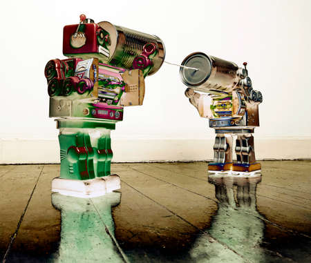 Two retro  Robots toys talking on tin can phones on an old wooden floorの写真素材