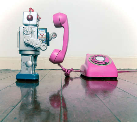 big silver robot toy on  a pink  phone standing on an old wooden floor toned imageの写真素材