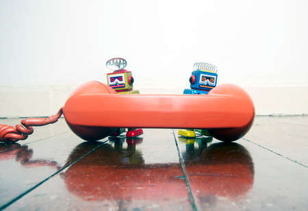 two little retro robots on the phone  on a old wooden floor with reflection toned imageの写真素材