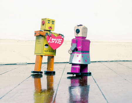 retro yellow robot showing love with a red  love heart  standing on a old wooden floorの写真素材