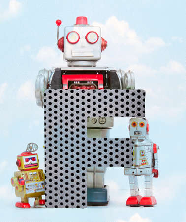 retro robots holding a big  metal letter F with blue sky and cloudsの写真素材