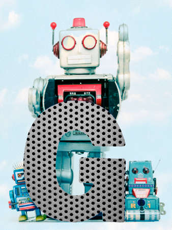 retro robots holding a big  metal letter G with blue sky and cloudsの写真素材