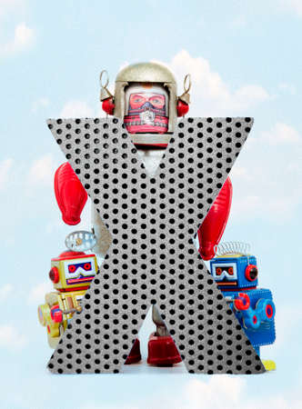 retro robots holding a big  metal letter  X with blue sky and cloudsの写真素材