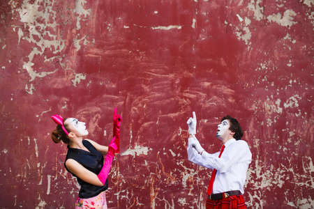 Couple mimes point to the top on a red wall.の写真素材