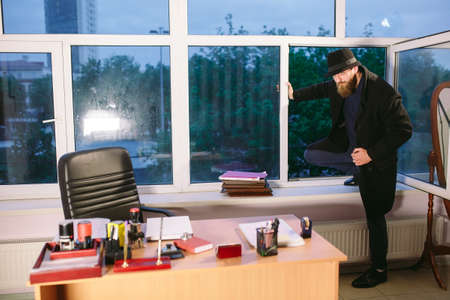 Concept. The thief comes into the office through the window. Thief in the officeの写真素材