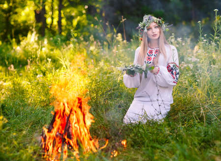 Midsummer. Woman weaving a wreath near the fire.の写真素材