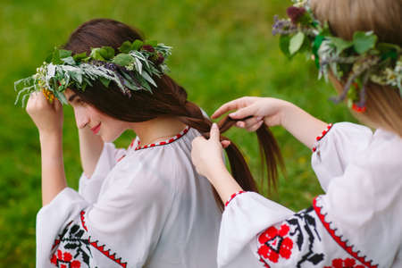 Midsummer. Two girls in the Slavic clothes weave braids in the hair near the fireの写真素材