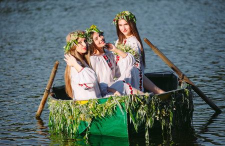 Midsummer. Young Girls in national costumes sail in a boat that is decorated with leaves and...