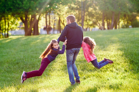 Father plays with daughters outdoors in a forest.