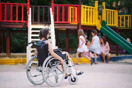 A girl with a broken leg sits in a wheelchair in front of the playground.の写真素材