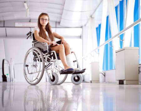 A young girl in a wheelchair is reading a book. Patient in a wheelchair in the hospital corridor.の写真素材