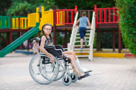 A girl with a broken leg sits in a wheelchair in front of the playgroundの写真素材