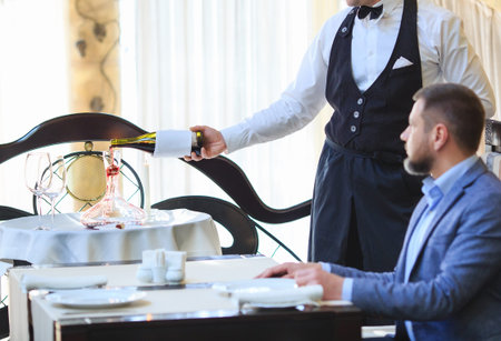 The sommelier pours the wine into the decanter near the guest in the restaurant
