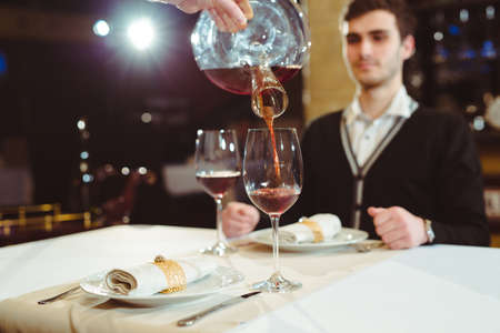 Waiter pouring red wine in a glass at a restaurant table.の写真素材