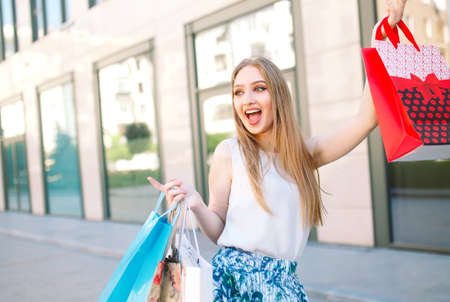 Lifestyle portrait young blonde girl, with shopping bags walking out from shopの写真素材