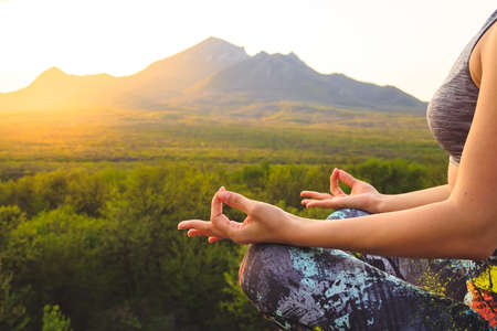 Young woman practicing yoga or pilates at sunset or sunrise in beautiful mountain location.の写真素材