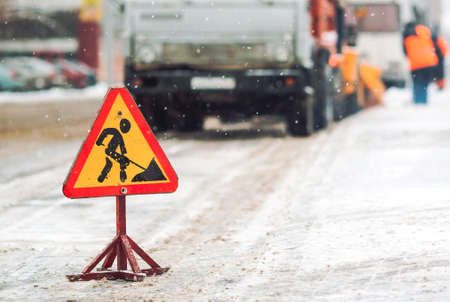 Snow-plow remove snow from the city street.Warning road sign.Winter service vehicle snow blower work.Cleaning snowy frozen roads.の写真素材