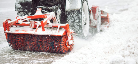 City service cleaning snow , a small tractor with a rotating brush clears a road in the city park...