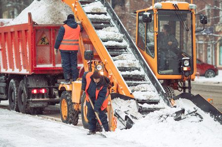 Snow cleaning tractor snow-removal machine loading pile of snow on a dump truck. Snow plow outdoors...