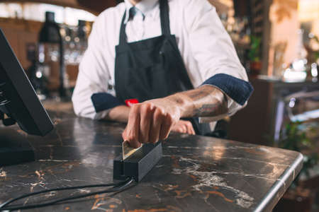 small business, people and service concept - happy man or waiter in apron at counter with cashbox working at bar or coffee shopの写真素材