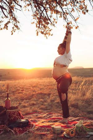 Pregnant woman doing yoga in the field at sunset. Girl holding a dream catcher and doing exerciseの写真素材