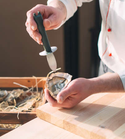 Opening the hollow and flat oysters. Chef opens oysters in the restaurantの写真素材