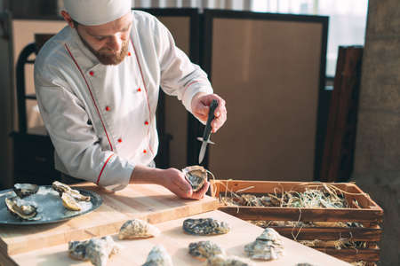 Opening the hollow and flat oysters. Chef opens oysters in the restaurant.の写真素材