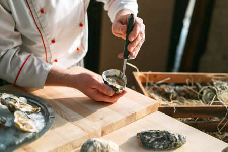 Opening the hollow and flat oysters. Chef opens oysters in the restaurant.の写真素材