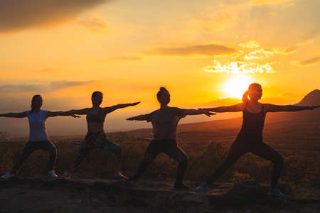 Silhouette of young womans practicing yoga or pilates at sunset or sunrise in beautiful mountain location.の写真素材