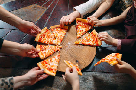 Hands taking pizza slices from wooden table, close up viewの写真素材