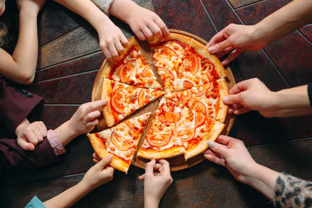 Hands taking pizza slices from wooden table, close up view.の写真素材