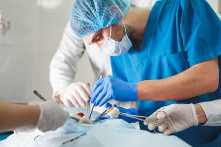 Group of surgeons at work operating in surgical theatre. Resuscitation medicine team wearing protective masks holding steel medical toolsの写真素材