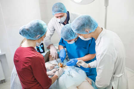 Group of surgeons at work operating in surgical theatre. Resuscitation medicine team wearing protective masks holding steel medical toolsの写真素材