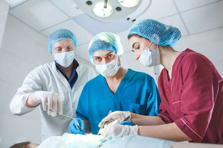 Group of surgeons at work operating in surgical theatre. Resuscitation medicine team wearing protective masks holding steel medical toolsの写真素材