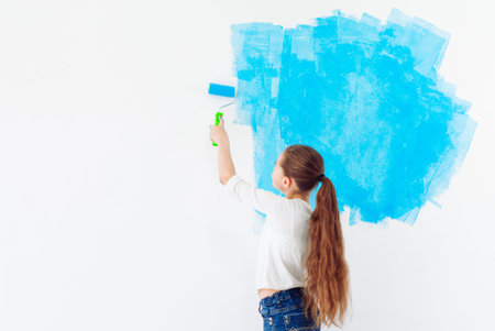 Repair in the apartment. Happy child girl paints the wall with blue paint,