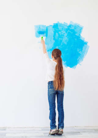 Repair in the apartment. Happy child girl paints the wall with blue paint,の写真素材