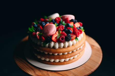 Fruit cake. Cake decorated with berries on a wooden stand on a black backgroundの写真素材