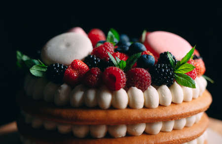 Fruit cake. Cake decorated with berries on a wooden stand on a black backgroundの写真素材