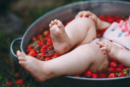 A little girl bathes in a basin with strawberries in the garden.