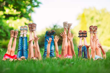 Children lying on green grass in park on a summer day with their legs lifted up to the sky.の写真素材