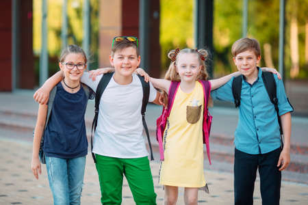 Childrens friendship. Four little school students, two boys and two girls, stand in an embrace on the schoolyard.の写真素材