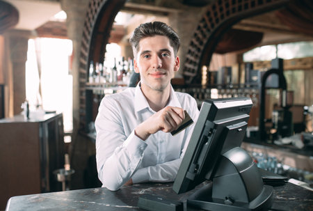 small business, people and service concept - happy man or waiter in apron at counter with cashbox...