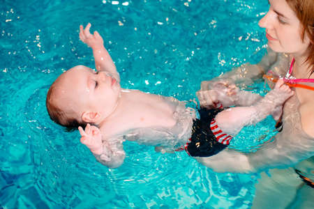 A group of mothers with their young children in a childrens swimming class with a coach.の写真素材