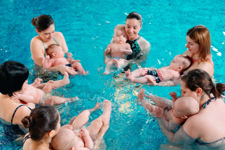 A group of mothers with their young children in a childrens swimming class with a coach.の写真素材