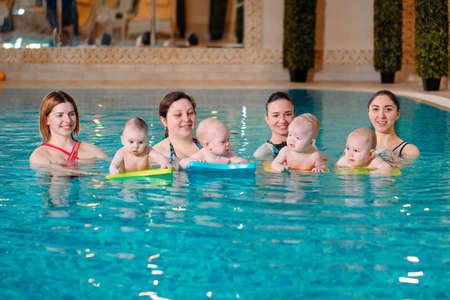 A group of mothers with their young children in a childrens swimming class with a coach.の写真素材
